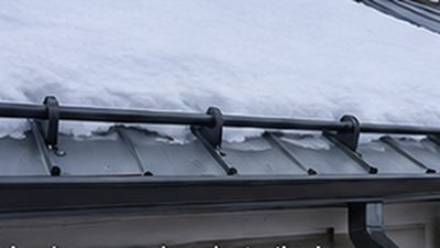 Snow retention bar installed above an entry door on a standing seam metal roof